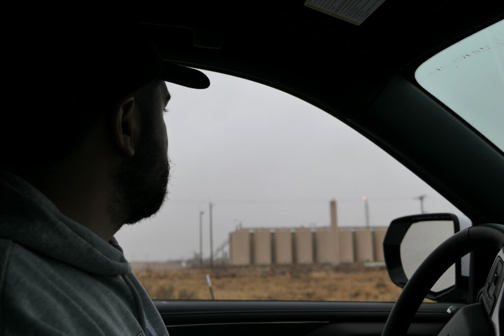 Miguel Escoto of Oilfield Witness observes a flare in the background behind a line of storage tanks near Pecos, Texas on March 16. Escoto has conducted methane monitoring in the Permian Basin since 2020. Credit: Martha Pskowski/Inside Climate News