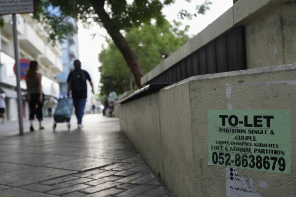 People walk past a concrete bench plastered with advertisements for inexpensive, partitioned housing in Dubai, United Arab Emirates, Friday, July 4, 2025. (AP Photo/Altaf Qadri)