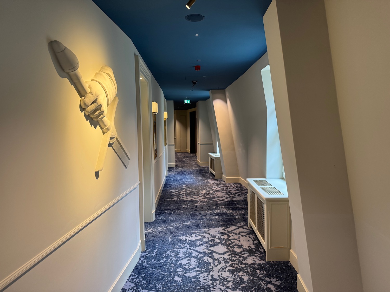 a hallway with a blue ceiling and a white wall with a hand holding a sword