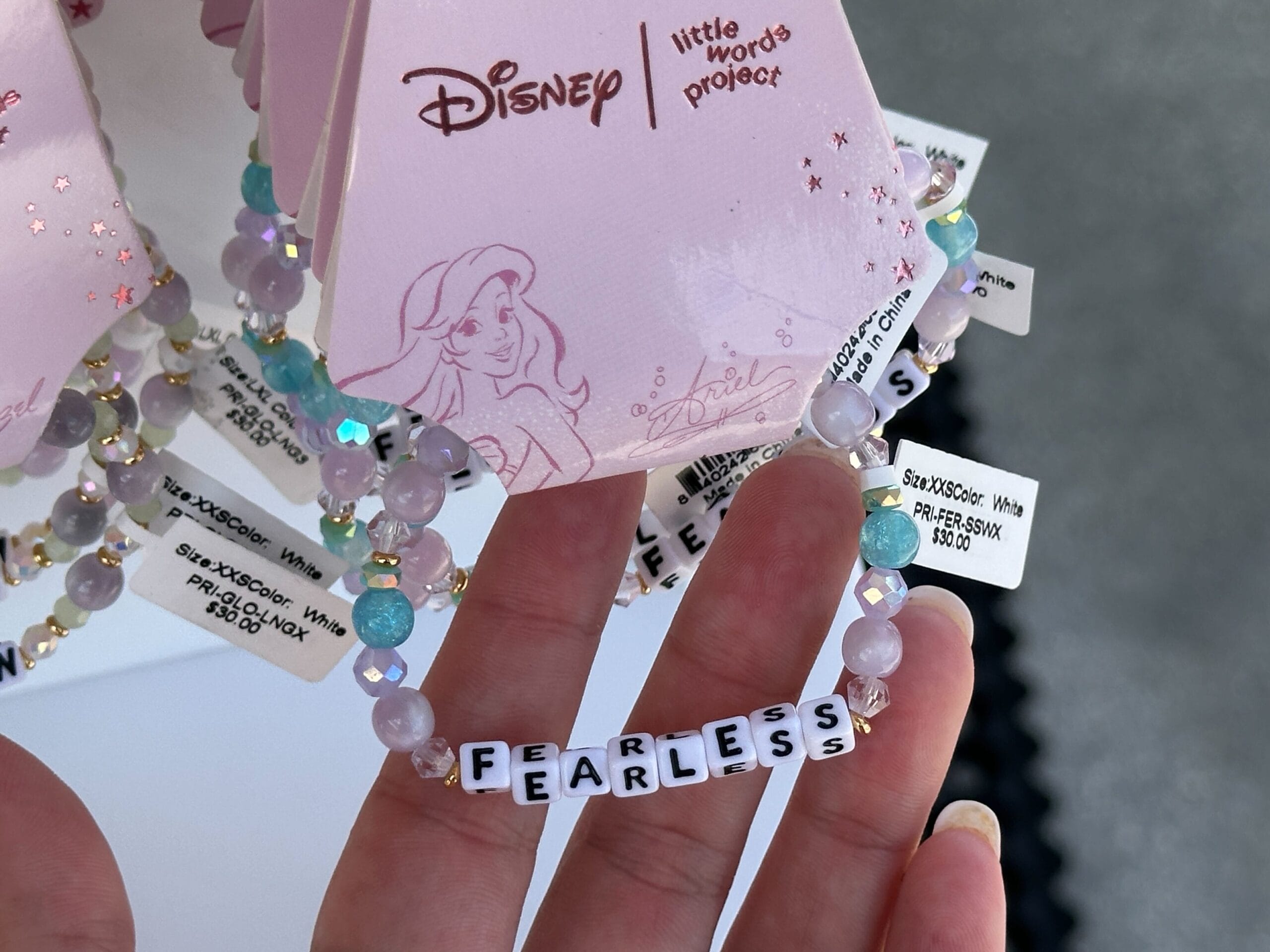 A hand holds a beaded Disney bracelet that spells