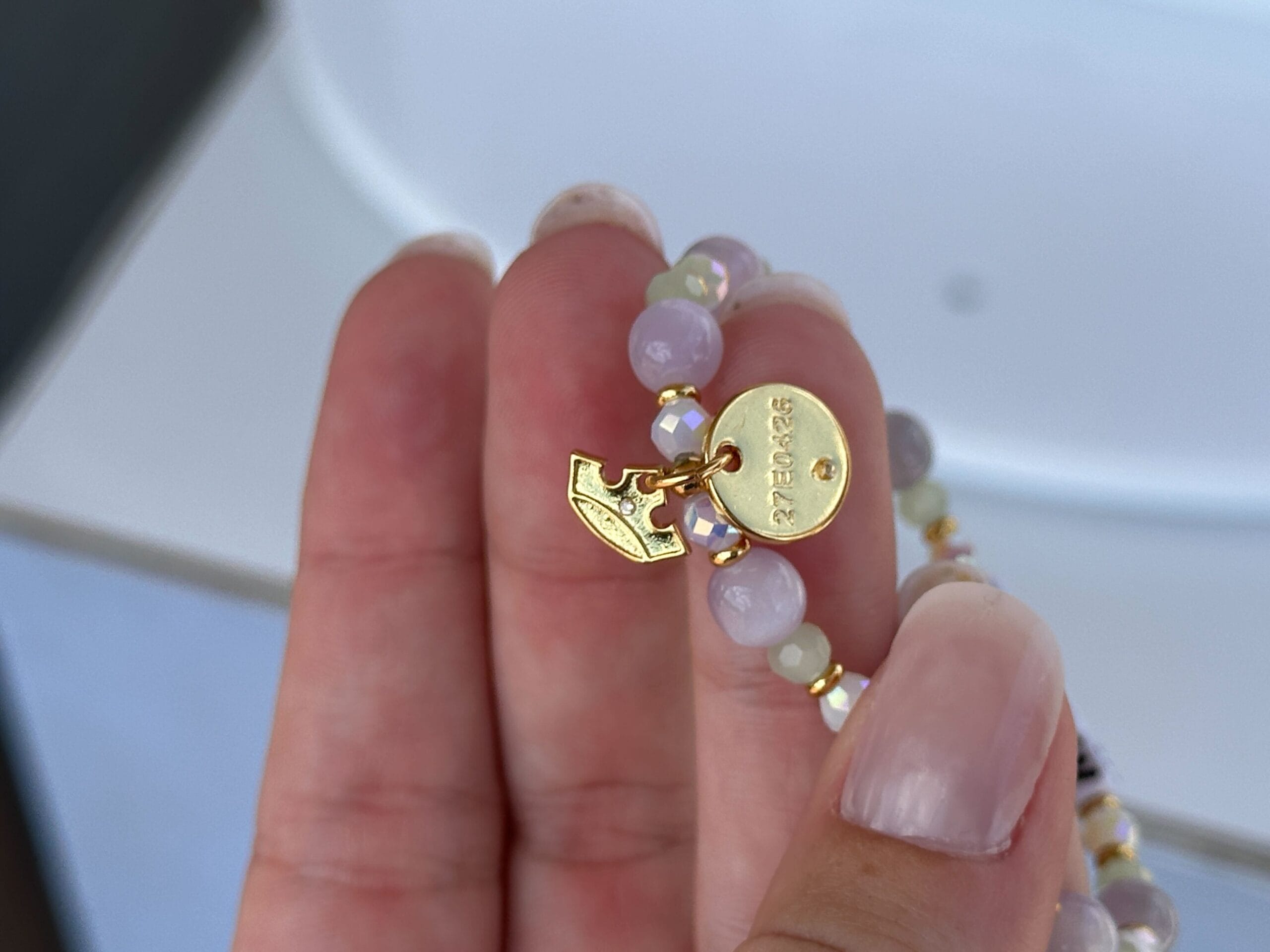 A hand holds a beaded bracelet with a gold oval tag engraved