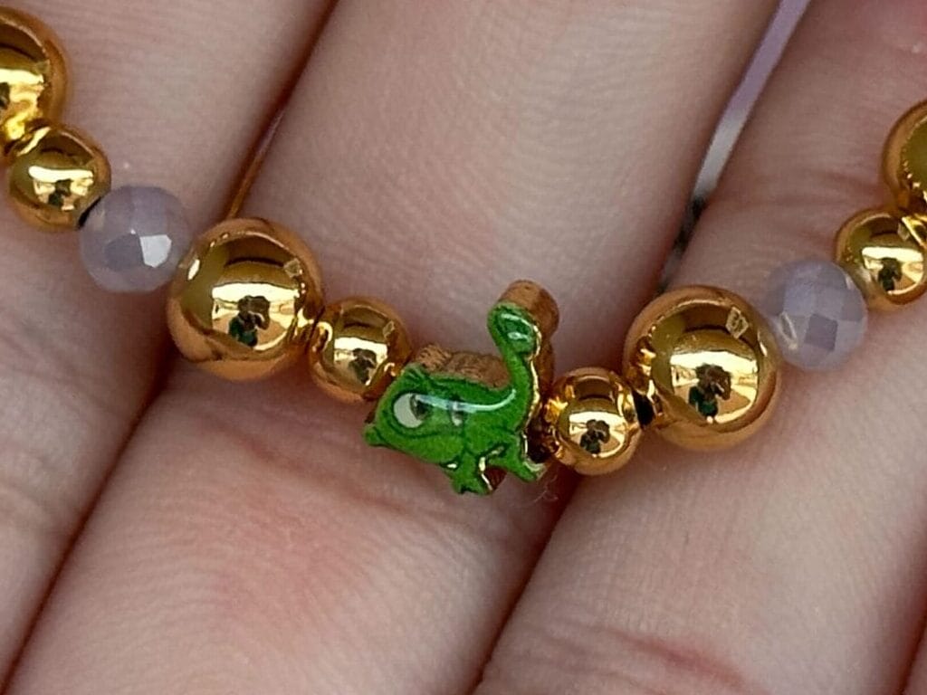 Hand holding a Disney Rapunzel bracelet with gold beads and a green accent, displayed on pink packaging.