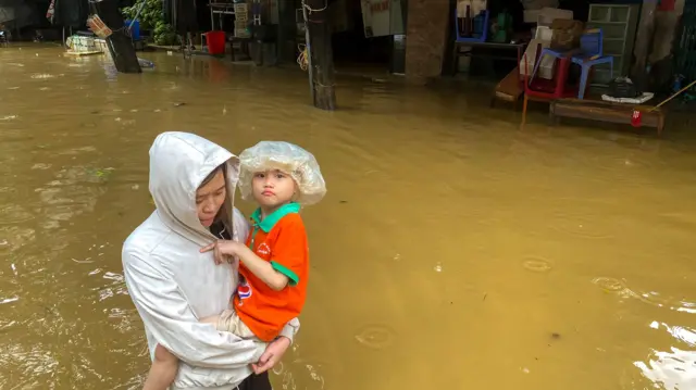 台风摩羯吹袭过后越南太原市一位女士抱着小男孩在淹水街道上涉水而行（11/9/2024）
